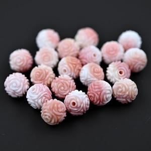 Puede incluir: Una colección de cuentas de concha rosa y blanca con un diseño de rosa. Las cuentas están talladas en concha y tienen un acabado liso y pulido.