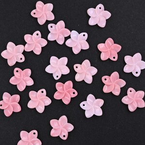 May include: A collection of small, light pink, five-petaled flower charms. Each individual charm features a smooth, glossy finish and a single small hole at the top of one petal, designed for threading or attachment in jewelry making projects.