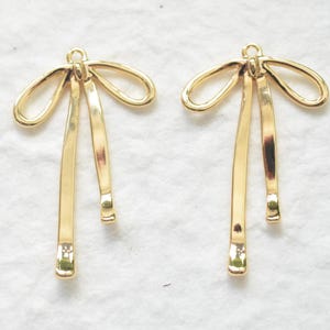 Op de afbeelding: Een paar gouden metalen boog oorringen met een hangend ontwerp. De bogen zijn gemaakt van twee lussen die in het midden met elkaar verbonden zijn. De oorringen hebben een eenvoudig en elegant ontwerp.