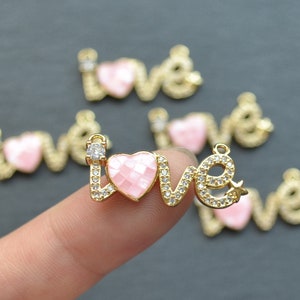 Pode incluir: Encanto 'LOVE' em tom dourado com um coração rosa e strass transparentes. O encanto é perfeito para a elaboração de joias ou para adicionar um toque de brilho às suas manualidades.