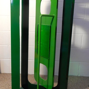 May include: A green metal sculpture with three rectangular frames, one inside the other, creating a geometric design. The sculpture is standing on a green base.