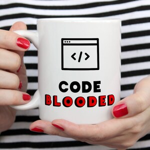 May include: White ceramic mug featuring a black and white illustration of a computer screen with code symbols and the text "CODE BLOODED" in red lettering.