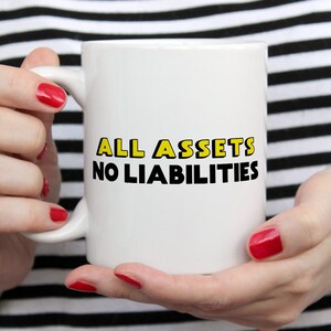 May include: White ceramic mug with black text that reads "ALL ASSETS NO LIABILITIES" in yellow outlined letters.