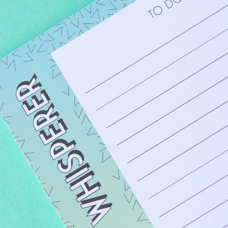 May include: A white to-do list notepad with a blue and green gradient background. The background has a pattern of small white triangles. The text "Whisperer" is printed in black on the left side of the notepad.