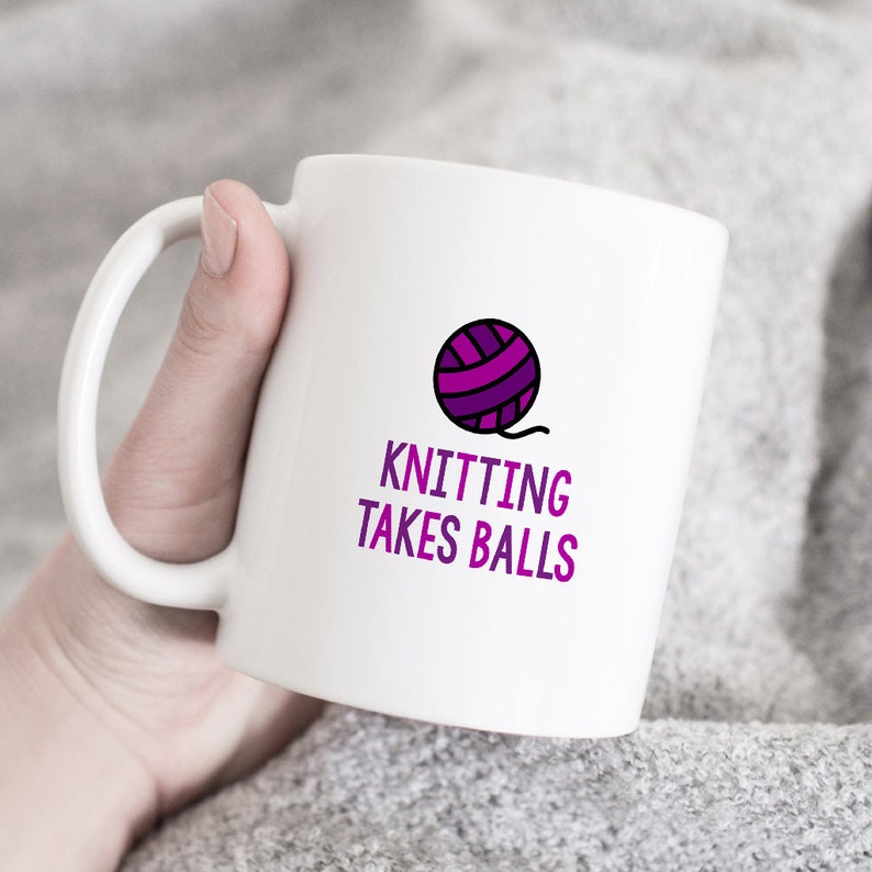 May include: White ceramic mug with a purple yarn ball graphic and the text "Knitting Takes Balls".