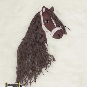 Könnte beinhalten: Braunes Pferdekopf-Applique mit einem weißen floralen Zaumzeug. Die Mähne des Pferdes ist lang und fließend.