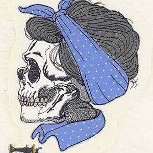 Könnte beinhalten: Ein gestickter Schädel in Schwarzweiß mit einem blauen Bandana mit weißen Punkten, das um den Kopf gebunden ist. Das Bandana ist am Hinterkopf des Schädels zu einem Knoten gebunden.