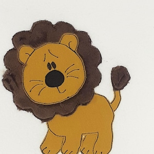 Könnte beinhalten: Eine braune und beigefarbene Löwenapplikation mit einer braunen Mähne. Der Löwe hat eine schwarze Nase und einen lächelnden Mund.