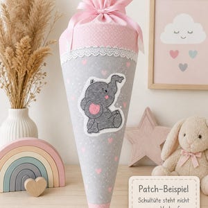 Könnte beinhalten: Eine graue und rosa Schultüte mit einem niedlichen Elefanten-Patch. Der Kegel ist mit rosa Herzen und einer weißen Spitzenborte verziert. Die Spitze ist mit einem rosa Band gebunden und mit rosa Pünktchenstoff gefüllt.