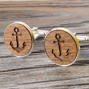 May include: A pair of silver cufflinks with a round wooden inlay featuring a carved anchor design.