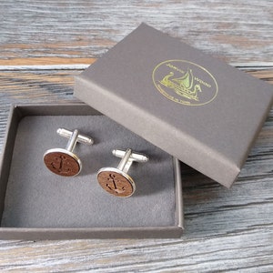 May include: A pair of wooden cufflinks with an anchor design in a grey box. The box has a gold label with the text "J&oslash;rvik Wood Handmade in Latvia".