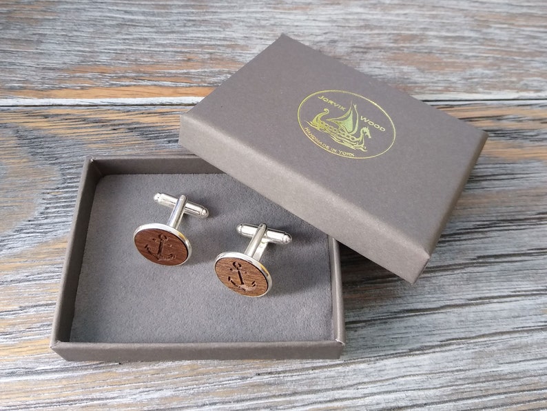 May include: A pair of wooden cufflinks with an anchor design in a grey box. The box has a gold label with the text "J&oslash;rvik Wood Handmade in Latvia".