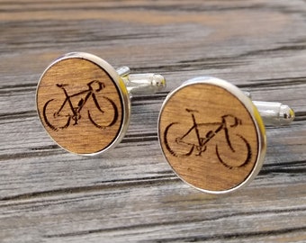 May include: A pair of wooden cufflinks with a silver metal backing. Each cufflink features a laser-engraved image of a bicycle.
