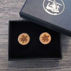 Può includere: Due gemelli in legno in una scatola nera. Ogni gemello presenta un design inciso a laser di una tartaruga marina.