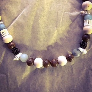 May include: A necklace made of wood, white and blue beads, and seashells. The necklace has a natural, earthy feel.
