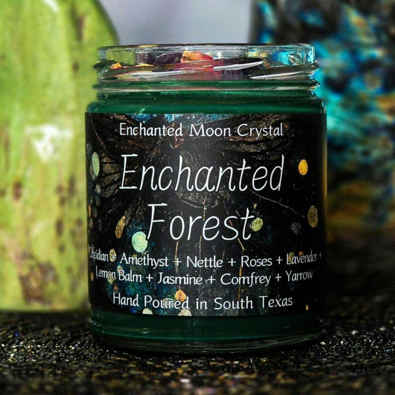 Może przedstawiać: Zielony szklany słoik z czarną etykietą z napisem "Enchanted Forest" w białym skrypcie. Etykieta zawiera składniki takie jak ametyst i lawenda. Widoczny jest r&oacute;wnież tekst "Hand Poured in South Texas".