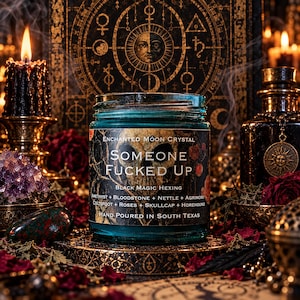 Someone Fucked Up black magic candle displayed on a lavish gothic witchcraft altar with ornate golden occult symbols, burning black candles, amethyst crystals, dried red roses, and delicate incense smoke. The turquoise glass candle jar features a dark hexing-themed label, illuminated by dramatic amber candlelight. A mystical ritual setting inspired by banishing magic, spiritual protection, and personal empowerment.
