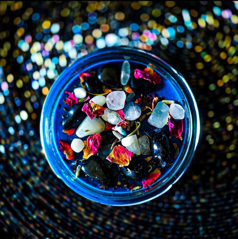 Top view of the deep blue Hecate candle decorated with pale Moonstone, Lavender, Mugwort, Thyme, and Rosemary. White stones and colorful dried botanicals contrast beautifully against the rich blue wax. Keywords: Hecate candle, ritual candle, witchcraft.