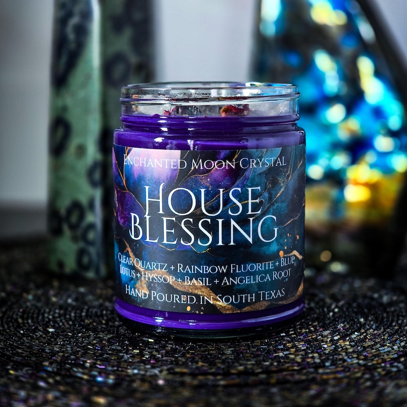 Pu&ograve; includere: Una candela in barattolo di vetro con cera viola scuro e un'etichetta che recita "ENCHANTED MOON CRYSTAL HOUSE BLESSING". L'etichetta presenta un design celeste blu scuro e viola. La candela include quarzo trasparente, fluorite arcobaleno, loto blu, issopo, basilico e radice di angelica.