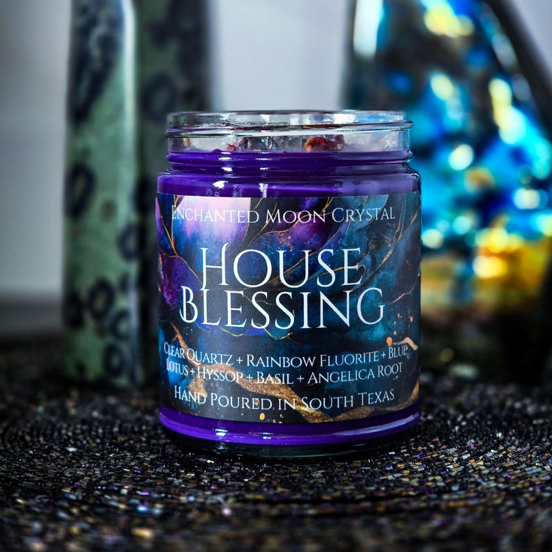 Pu&ograve; includere: Una candela in barattolo di vetro con cera viola e un'etichetta che recita "ENCHANTED MOON CRYSTAL HOUSE BLESSING". L'etichetta presenta un design blu scuro e viola con accenti dorati. La candela &egrave; versata a mano in Texas.