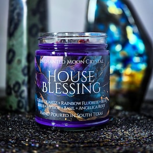 Pu&ograve; includere: Una candela in barattolo di vetro viola con la scritta "ENCHANTED MOON CRYSTAL HOUSE BLESSING". L'etichetta elenca ingredienti tra cui quarzo trasparente, fluorite arcobaleno e loto. La candela &egrave; versata a mano nel Texas del Sud.