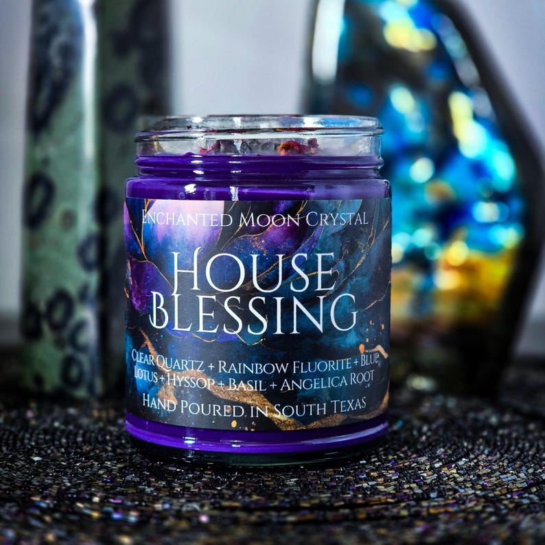 Pu&ograve; includere: Una candela in barattolo di vetro viola con la scritta "ENCHANTED MOON CRYSTAL HOUSE BLESSING". L'etichetta elenca ingredienti tra cui quarzo trasparente, fluorite arcobaleno e loto. La candela &egrave; versata a mano nel Texas del Sud.