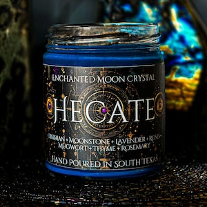 Deep blue Hecate intention candle in a clear glass jar with a dark celestial label and mystical gold details. Hand dressed with Moonstone, Lavender, Mugwort, Thyme, and Rosemary. A handmade spiritual candle inspired by Hecate, witchcraft, intuition, and transformation.