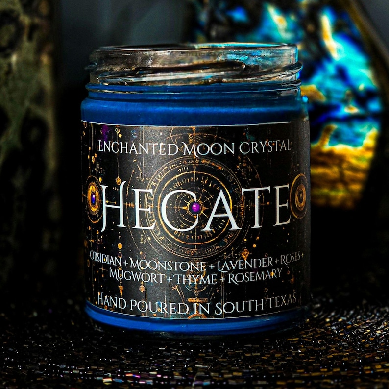 Deep blue Hecate intention candle in a clear glass jar with a dark celestial label and mystical gold details. Hand dressed with Moonstone, Lavender, Mugwort, Thyme, and Rosemary. A handmade spiritual candle inspired by Hecate, witchcraft, intuition, and transformation.