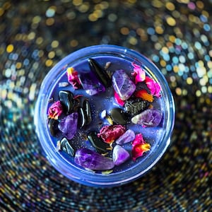 Close overhead view of Witching Hour candle with black tourmaline, dried roses, lavender and ritual botanicals against a shimmering background.