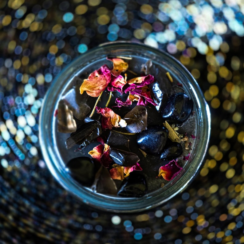 Overhead view of the Season of the Witch candle topped with smoky quartz, obsidian and colorful dried botanicals over deep black wax. Handmade witch candle featuring crystals and herbs associated with protection, grounding, ritual work and divination.