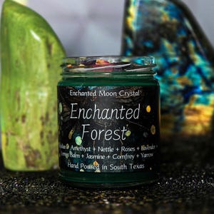 Może przedstawiać: Zielony szklany słoik z czarną etykietą z napisem "Enchanted Forest". Etykieta zawiera składniki takie jak ametyst, pokrzywa i lawenda. Słoik jest wypełniony zieloną substancją i zwieńczony kolorowymi kawałkami. Widoczny jest r&oacute;wnież tekst "Hand Poured in South Texas".