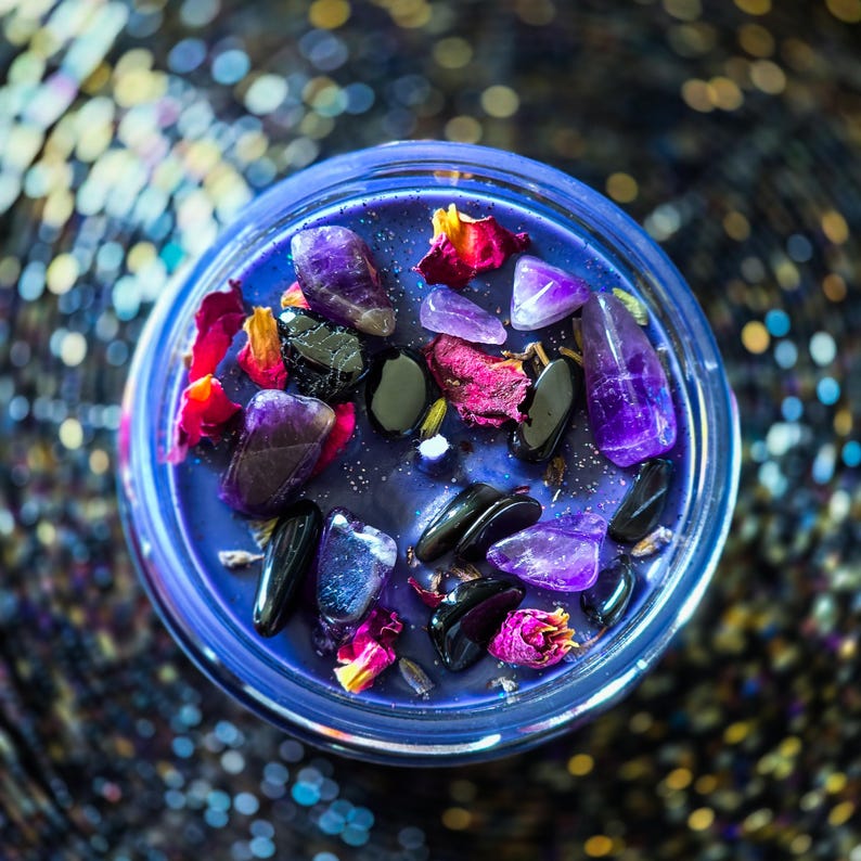 Overhead view of Witching Hour candle topped with black tourmaline, colorful rose petals, lavender and botanicals against a sparkling dark background.