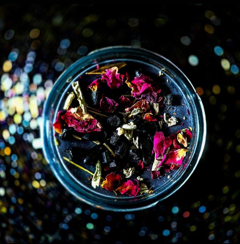 Overhead view of the Banishing candle showing dark wax decorated with colorful dried botanicals, herbs and crystals surrounding the wick. A handmade spiritual cleansing candle created for banishing, cord cutting, energy clearing and releasing unwanted attachments.