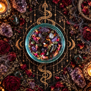 Direct top view of the Someone Fucked Up black magic candle positioned over a striking golden serpent-inspired occult symbol. The turquoise glass vessel contains dark wax adorned with polished crystals, colorful rose petals, dried lavender, and botanical ingredients. Burgundy roses, amethyst clusters, and glowing candles surround the jar, creating a mystical altar arrangement with rich gothic detailing.