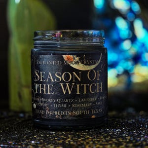 Season of the Witch candle photographed against a dark mystical background with luminous blue and green accents. Black wax and a vintage botanical label create a moody witchy aesthetic for this handmade ritual and intention candle.