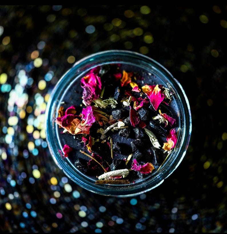 Close overhead view of the Banishing intention candle, featuring dark wax topped with dried flowers, herbs and crystals. Designed for energetic cleansing, banishing negative energy, severing unwanted ties and creating a protected, cleared space.