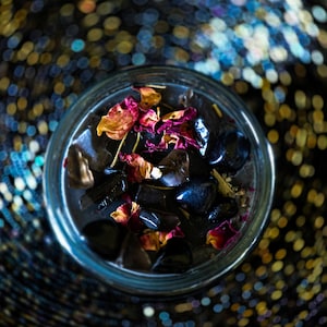 Detailed top view of the Season of the Witch candle with black wax, polished smoky quartz and obsidian stones, dried flowers and ritual herbs. A richly decorated witchcraft candle inspired by grounding, protection, meditation, divination and spellwork.