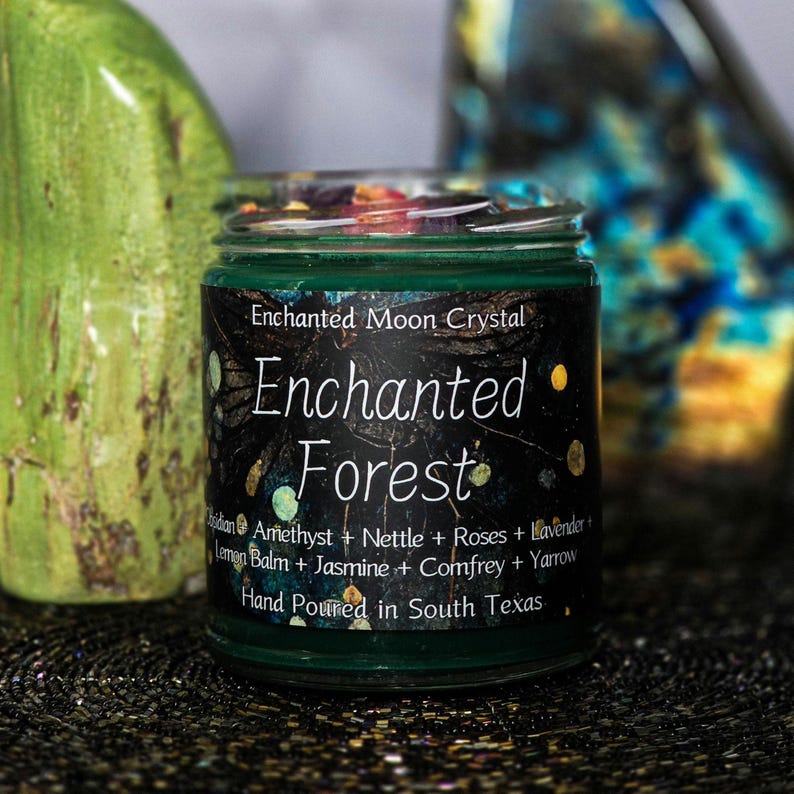 Może przedstawiać: Mały szklany słoik z zieloną etykietą z napisem "Enchanted Forest". Etykieta zawiera r&oacute;wnież składniki takie jak ametyst, lawenda i jaśmin. Słoik jest ręcznie nalewany w południowym Teksasie.