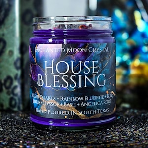May include: A glass jar candle with a deep purple wax and a label that reads "ENCHANTED MOON CRYSTAL HOUSE BLESSING." The label features a cosmic design with gold accents and ingredient details. The candle is hand-poured in South Texas.