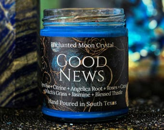 May include: A blue candle in a glass jar with a black label featuring gold floral patterns and the text: Enchanted Moon Crystal, GOOD NEWS, Tigers Eye + Citrine + Angelica Root + Roses + Catnip + Witch's Grass + Jasmine + Blessed Thistle, Hand Poured in South Texas.
