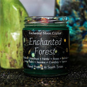 Może przedstawiać: Mały szklany słoik z zieloną etykietą z napisem "Enchanted Forest". Etykieta zawiera składniki takie jak ametyst, pokrzywa i lawenda. Widoczny jest r&oacute;wnież tekst "Hand Poured in South Texas".