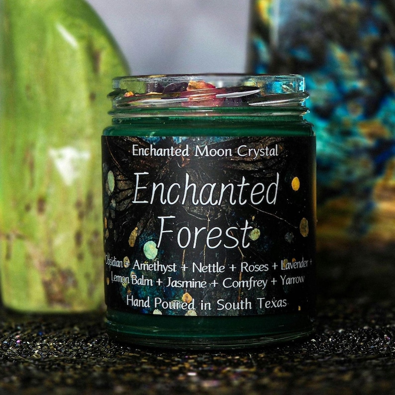 Może przedstawiać: Mały szklany słoik z zieloną etykietą z napisem "Enchanted Forest". Etykieta zawiera składniki takie jak ametyst, pokrzywa i lawenda. Widoczny jest r&oacute;wnież tekst "Hand Poured in South Texas".
