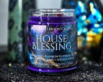 May include: A purple candle in a glass jar with a label reading Enchanted Moon Crystal House Blessing, Clear Quartz, Rainbow Fluorite, Blue Lotus, Hyssop, Basil, Angelica Root, and Hand Poured in South Texas with a dark marbled design.