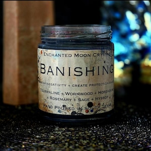 Front view of a handmade Banishing candle with dark wax in a glass jar and an aged parchment-style label. Created as an intention candle for removing unwanted energy, spiritual cleansing, protection and releasing energetic ties that no longer serve you