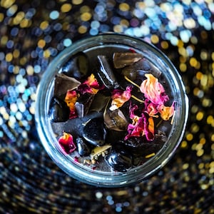 Close overhead photo of the Season of the Witch candle featuring glossy black wax decorated with smoky quartz, obsidian, dried rose petals and herbal botanicals. Dark witch candle handcrafted for ritual, spellwork, protection, grounding and spiritual practice.