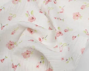 May include: White fabric with a delicate floral pattern. The fabric is adorned with small pink flowers and green leaves, creating a soft and feminine design. The fabric appears to be lightweight and flowing, suitable for various craft projects.