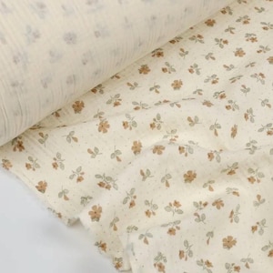 May include: A roll of cream-colored fabric with a floral pattern. The fabric features small, brown flowers and gray leaves scattered across a dotted background. The fabric is likely cotton or a similar material.