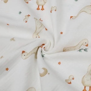May include: White fabric with a repeating pattern of watercolor geese in various poses, along with stars, moons, and sprigs of greenery. The geese are beige with orange beaks and feet. A soft, whimsical design.