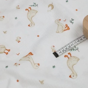 May include: White fabric with a repeating pattern of geese, ducklings, and botanical elements in shades of beige, orange, and green. A wooden spool with a dress form icon and a measuring tape are also visible.