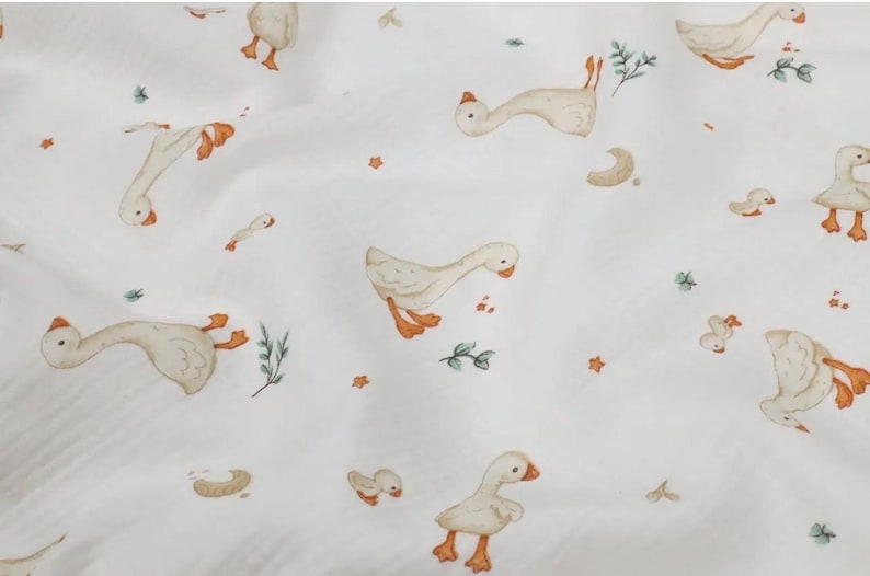 May include: White fabric with a repeating pattern of geese in various poses. The geese are depicted in shades of beige, with orange feet and beaks. Small green sprigs and orange star shapes are scattered across the fabric.